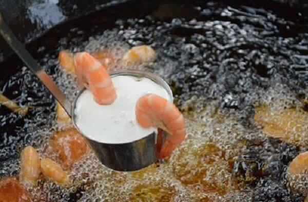 Tiếp đó bạn lựa 1 con tôm để nhẹ lên trên rồi nhúng từ từ cái muôi vào chảo dầu đang sôi trên lửa nhỏ.